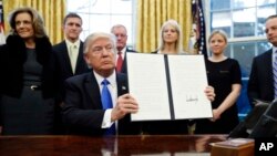 President Donald Trump holds up a signed executive order in the Oval Office of the White House in Washington, Jan. 28, 2017.