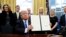 President Donald Trump holds up a signed executive order in the Oval Office of the White House in Washington, Jan. 28, 2017.