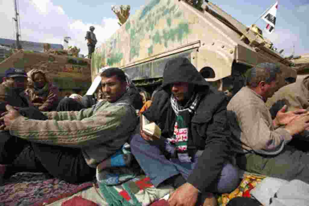A protester reads the Quran as they gather around army vehicles at Tahrir Square in Cairo, February 7, 2011
