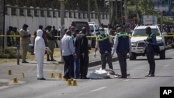 In this image from video, security officers and forensic experts stand near a covered body in a street in Dar es Salaam, Tanzania, Aug. 25, 2021. Four people were killed by a gunman later identified as Hamza Mohamed, a 33-year-old local resident. 