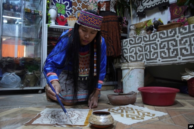 Sadith Silvano, from Paoyhan, a Shipibo-Konibo Indigenous community in the Amazon, paints a tablecloth at her home and workshop in Lima, Peru, Saturday, Oct. 19, 2024. (AP Photo/Guadalupe Pardo)