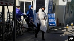 FILE - A woman carries a child as she and others leave a children's hospital in Beijing, China, Nov. 24, 2023. China on Sept. 8, 2024, indicated that it would allow for establishment of wholly foreign-owned hospitals in nine areas of the country, including the capital.