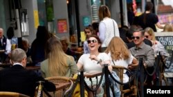 FILE - People relax at outdoor dining areas on the South Bank, as lockdown restrictions continue to ease amid the spread of the coronavirus disease, in London, May 28, 2021. 