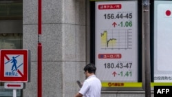 2026年8月3日，一名男子在东京一家证券公司显示美元兑日元汇率的标牌旁查看手机。