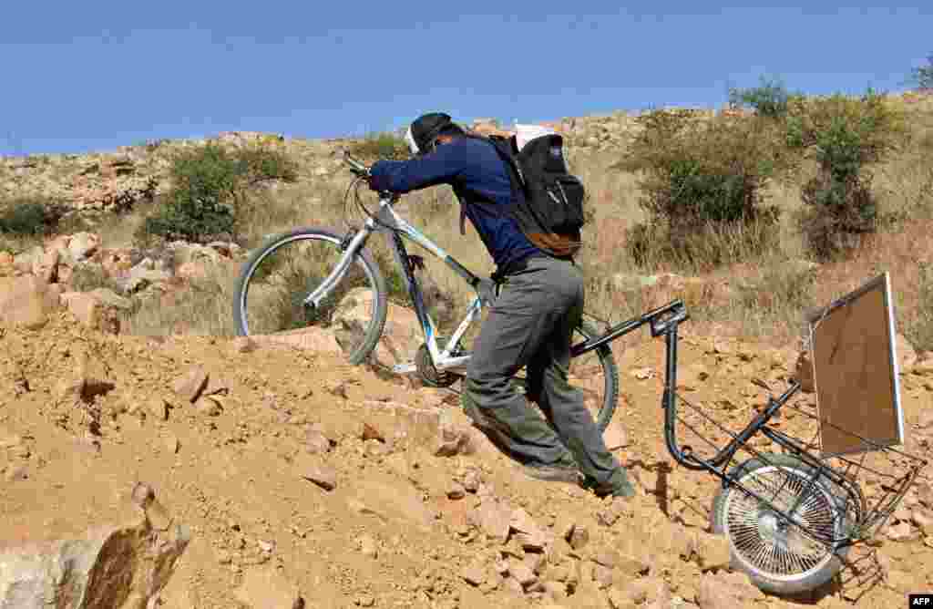 Bolivian teacher Wilfredo Negrete Jaldin pushes his bike carrying a board on his way to his students' homes in Aiquile.