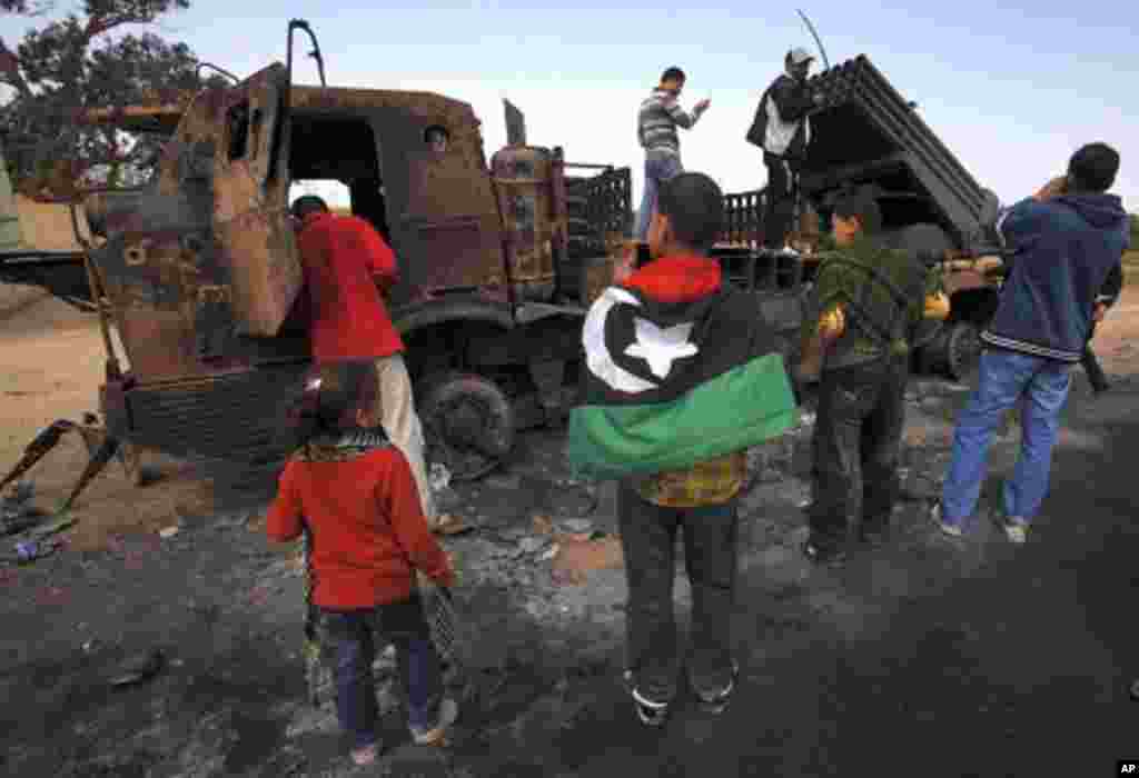 People look at weapons belonging to forces loyal to Libyan leader Muammar Gaddafi, destroyed by a coalition air strike, along a road between Benghazi and Ajdabiyah, March 23, 2011