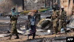 A Sudanese man carries a bed passes South Sudan People's Liberation Army (SPLA) national army soldiers in the Unity state capital, Bentiu, in January 2014.