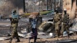 A Sudanese man carries a bed past South Sudan People's Liberation Army (SPLA) national army soldiers patroling the town of Bentiu in 2014. The SPLA said fresh fighting erupted in Bentiu and a town in Jonglei state on Wednesday, March 24, 2015.