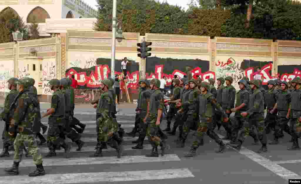 Soldiers march while anti-Mursi protesters paint a mural outside the Egyptian presidential palace in Cairo December 9, 2012.