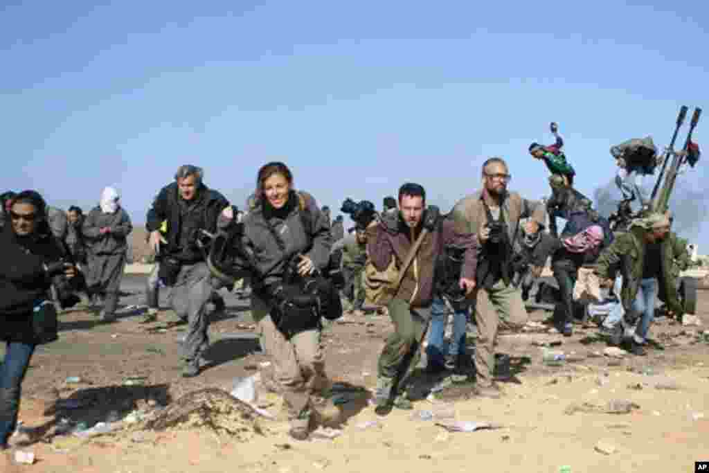 Journalists and photographers, including Hicks (R- in glasses) and Addario (far L), Moore (2nd L), Pickett (3rdL) and Poupin (4th L) run for cover during a bombing run by Libyan government planes at a checkpoint near the oil refinery of Ras Lanuf March 11