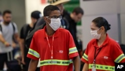 Airport employees wear masks as a precaution against the spread of the new coronavirus COVID-19 as they work at the Sao Paulo International Airport in Sao Paulo, Brazil, Feb. 26, 2020. 