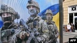A couple sits outside a cafe next to a military recruiting poster in Kyiv, Ukraine, on April 9, 2024.