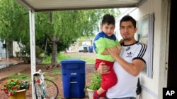 Osvaldo Salas, 29, stands with his son outside their home in suburban Phoenix on Wednesday, March 18, 2020. Salas, who isn't proficient in English, says he's disappointed state authorities haven't posted any information on the coronavirus in Spanish…