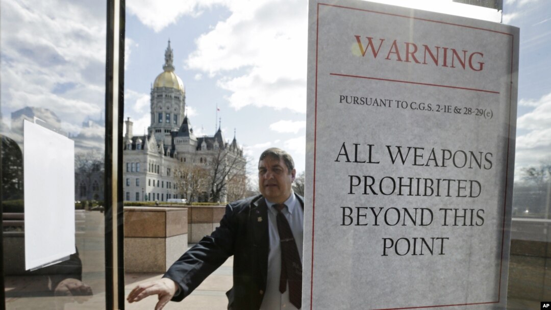 A Capitol security officer enters a revolving door at the legislative office building, with a sign warning not to bring weapons on to the grounds at the Capitol in Hartford, Conn., April 3, 2013. 