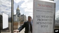 A Capitol security officer enters a revolving door at the legislative office building, with a sign warning not to bring weapons on to the grounds at the Capitol in Hartford, Conn., April 3, 2013. 