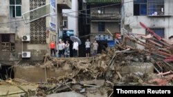 Residents stand on a bank of a river as they look at the rubble of a bridge damaged by flood following heavy rainfall in Nanjing, Fujian province, China, July 9, 2019.