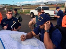 In this Coast Guard photo, Coast Guard responders look over a map of the Na Pali Coast State Wilderness Park on the Hawaiian island of Kauai, Dec. 27, 2019, the day after a tour helicopter disappeared with seven people aboard.