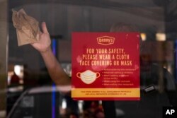 A restaurant worker cleans the door of a Denny's restaurant in Garden Grove, Calif., May 17, 2021. California won't lift its mask requirement until June 15 to give the public and businesses time to prepare.