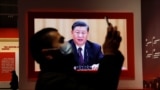 A visitor holds his mobile phone near a screen showing Chinese President Xi Jinping