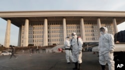 Workers wearing protective suits spray disinfectant as a precaution against the coronavirus at the National Assembly in Seoul, South Korea, Monday, Feb. 24, 2020. South Korea reported another large jump in new virus cases Monday a day after the the…