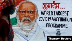 FILE PHOTO: A woman walks past a painting of Indian Prime Minister Narendra Modi a day before the inauguration of the COVID-19 vaccination drive on a street in Mumbai