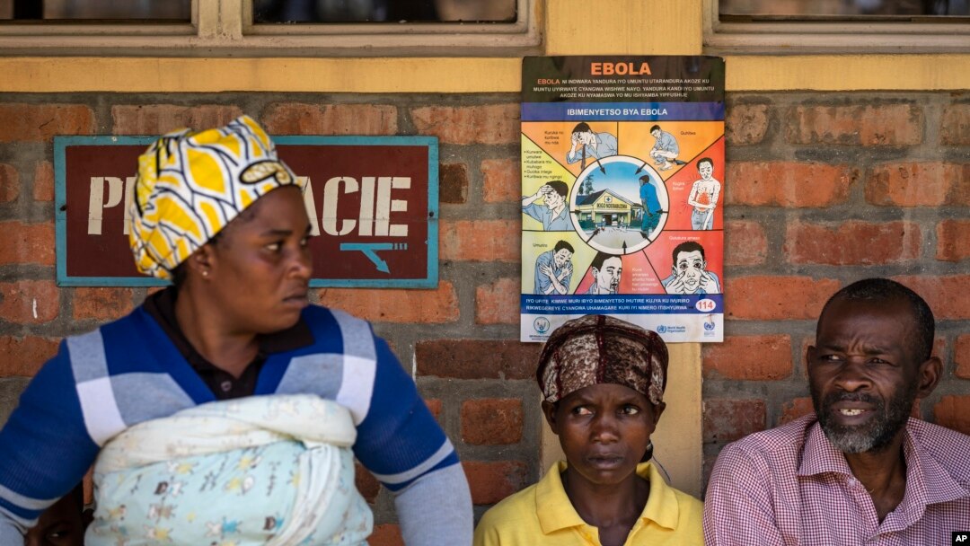 Patients waiting for prescriptions to be filled by the hospital pharmacy sit underneath a sign warning about the symptoms of Ebola, at Kibogora district hospital, near Lake Kivu and close to the border with Congo, in western Rwanda, Nov. 4, 2019.