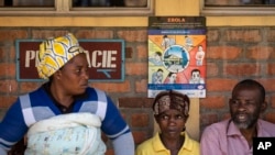 Patients waiting for prescriptions to be filled by the hospital pharmacy sit underneath a sign warning about the symptoms of Ebola, at Kibogora district hospital, near Lake Kivu and close to the border with Congo, in western Rwanda, Nov. 4, 2019.