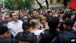 Kandidat dari partai oposisi Rusia dan pengacara di Yayasan untuk Pemberantasan Korupsi, Lyubov Sobol (tengah) dan kandidat Ivan Zhdanov (kedua dari kiri), berdiri bersama para pengunjuk rasa lainnya di depan garis polisi dalam unjuk rasa di Moskow, Rusia, Minggu, 14 Juli 2019.
