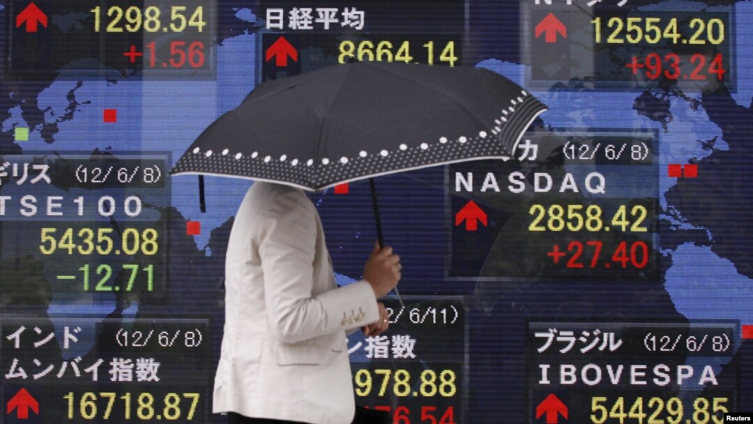 Seorang wanita melintasi layar elektronik yang menunjukkan kenaikan harga saham dunia di lantai bursa Tokyo (11/6).