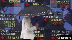 Una mujer se cubre de la lluvia mientras pasa frente al monitor del promedio Nikkei en Japón. Todavía no está claro las repercusiones de que Moody´s haya rebajado las calificaciones a 15 bancos a nivel mundial.