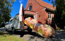 This photo provided by Ross Hall shows a cream doughnut-shaped coffin for the funeral of Phil McLean outside a church in Tauranga, New Zealand, on Feb 17, 2021. (Ross Hall via AP)