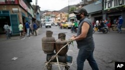 Un hombre que usa una tapabocas debido a la pandemia del coronavirus empuja una carriola con cilindros de gas vacíos en La Vega de Caracas, Venezuela.