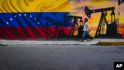 FILE - A man walks past a mural featuring oil pumps and wells in Caracas, Venezuela, May 21, 2022. 