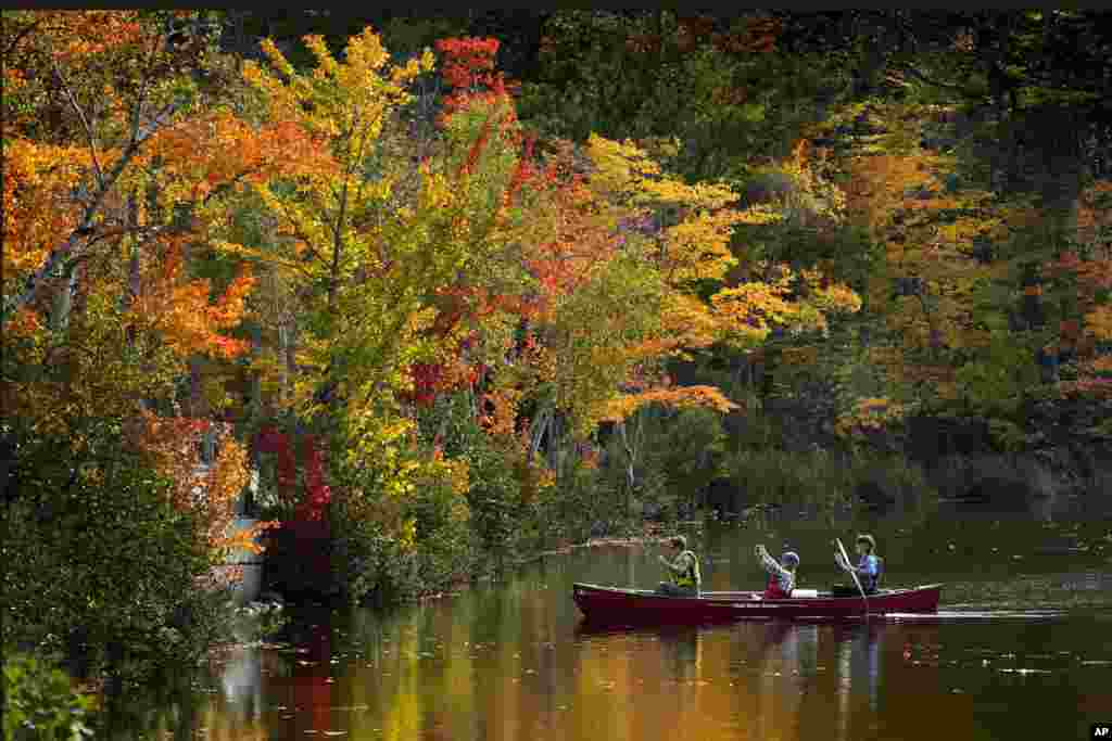 A passenger on a canoe photographs the brilliant fall foliage on South Pond, Oct. 9, 2021, in Bryant Point, Maine.