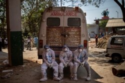 Exhausted workers, who bring dead bodies for cremation, sit on the rear step of an ambulance inside a crematorium, in New Delhi, India, April 24, 2021.