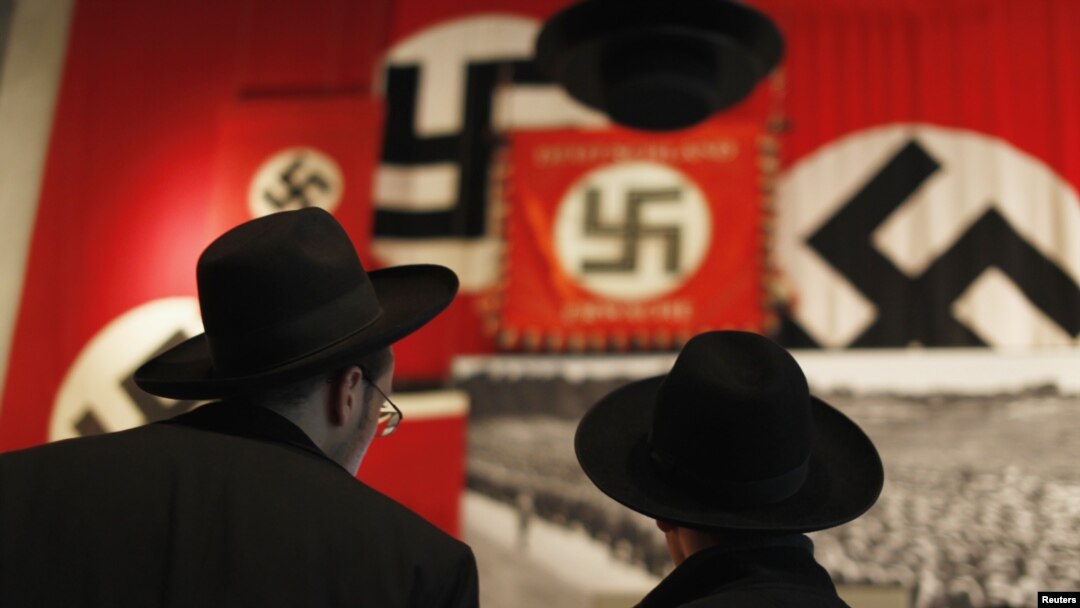 Para pengunjung Yahudi Ultra-Orthodox mengamati bendera Nazi yang dipasang di museum sejarah Holokos Yad Vashem di Yerusalem, 25 Januari 2013 (REUTERS/Amir Cohen). Majelis Umum PBB menetapkan tangal 27 Januari sebagai Hari Peringatan Holokos Internasional.