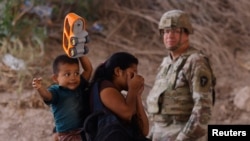 Una mujer, que carga con su hijo a la espalda, pasa frente a un militar de la Guardia Nacional de Texas tras haber cruzado el río Grande desde Ciudad Juárez, México, para pedir asilo en Estados Unidos, el 13 de mayo de 2023.