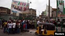 People crowd around a newsstand under election campaign posters for the All Progressives Congress (APC) (L) and presidential candidate of the APC Muhammadu Buhari (R) on a street in Lagos March 31, 2015. REUTERS/Joe Penney - RTR4VJWB