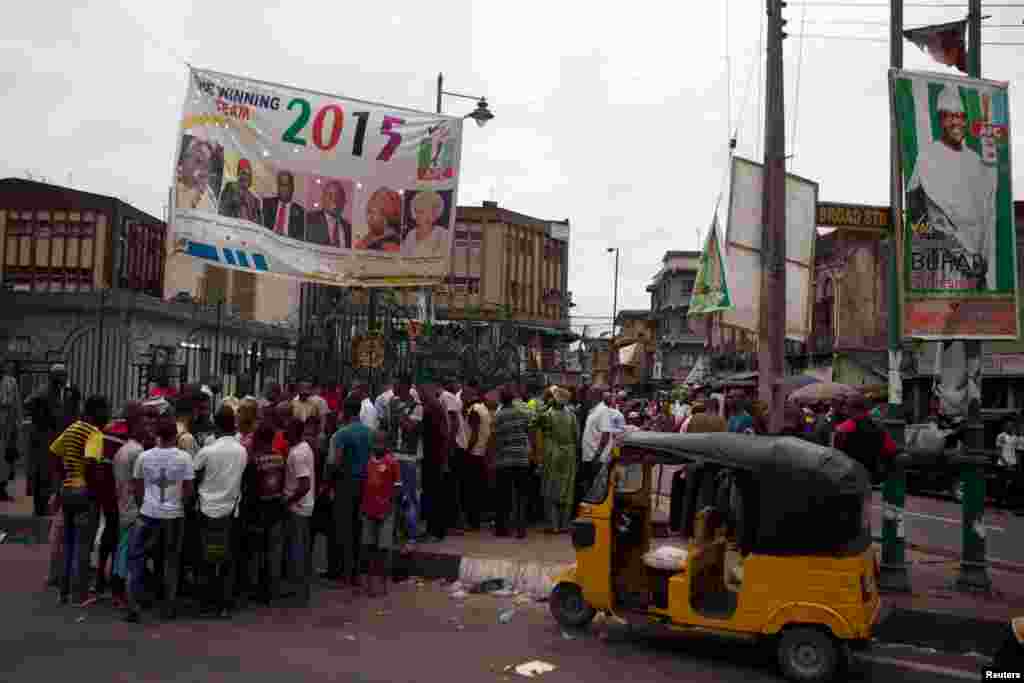 Warga mengerumuni kios surat kabar di bawah poster-poster kampanye pemilu untuk partai APC dan calon presiden APC, Muhammadu Buhari, di sebuah jalan di Lagos, Nigeria (31/3). (Reuters/Joe Penney)