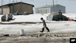 FILE - A young boy walks along the frozen banks of the Newtok River, in Newtok, Alaska, Wednesday, May 24, 2006, past frozen human waste dumped because the village lacks indoor plumbing.
