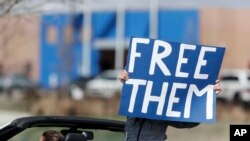 FILE - A protester wields a sign as anti-government groups call for the release of detained immigrants at the GEO Detention Center, because of the coronavirus, April 3, 2020, in Aurora, Colorado.