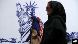 People walk past a satirical drawing of the Statue of Liberty after new anti-U.S. murals on the walls of the former U.S. Embassy were unveiled in a ceremony in Tehran, Iran, Nov. 2, 2019. 