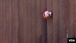 A person's hand reaches through a fenced section of the U.S.-Mexico border in southern California. (R. Taylor/VOA)