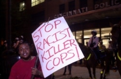 FILE - An anti-police protester stands in front of mounted Cincinnati Police, dressed in riot gear, outside police headquarters during a protest in Cincinnati, April 9, 2001.