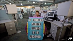 Un hombre sostiene una cometa con un mensaje que dice en español: "El Nacional seguirá impreso en un papagayo" en la sala de redacción del diario en Caracas, Venezuela. Diciembre 14, 2018. Foto: AP.