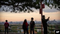 Varias personas con máscaras para protegerse del nuevo coronavirus observan el panorama desde un mirador en el tope de una colina en un parque público de Beijing, el sábado 25 de abril de 2020.