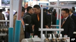 An exhibitor, center, talks to a visitor about his company's machine at the China Coal & Mining Expo in Beijing, Oct. 30, 2015. World Bank experts say economic growth will slow further in China this year.