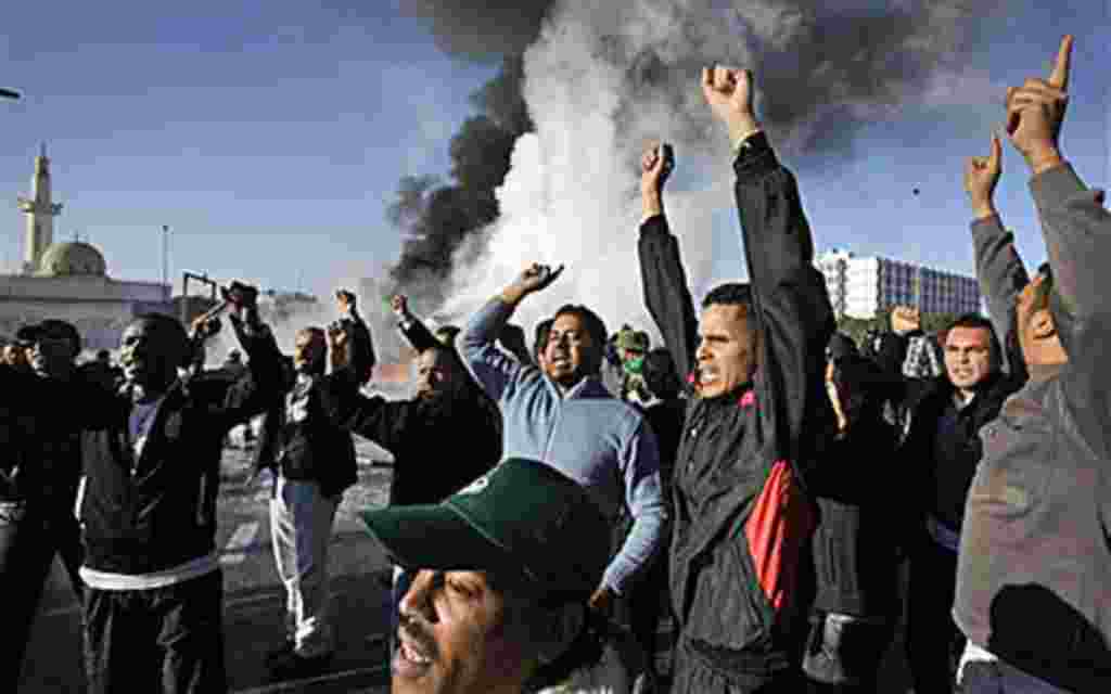 Manifestantes en respaldo a Gadhafi delante de una explosión de un tanque de crudo.