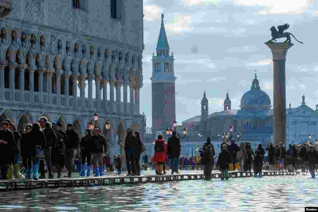 People walk through across a makeshift walkway over the flooded St. Mark&#39;s Square in Venice, Italy.