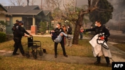 Police officers evacuate an elderly resident from her home during the Eaton Fire in Altadena, California, Jan. 8, 2025.